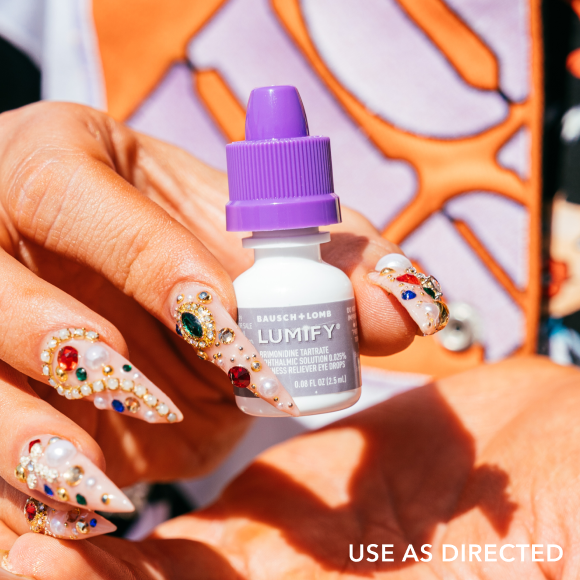 A hand holding up a Lumify eye drop bottle